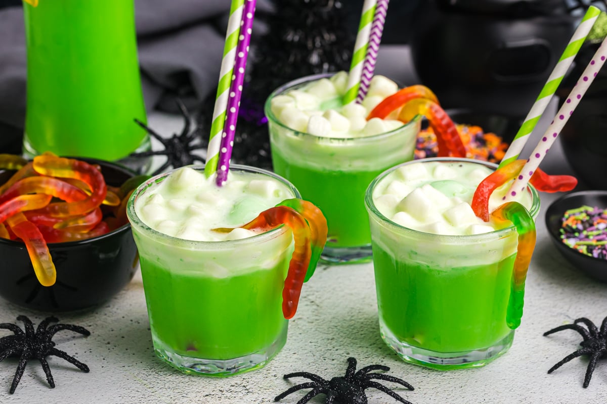 three cups of witches brew with gummy worms and straws