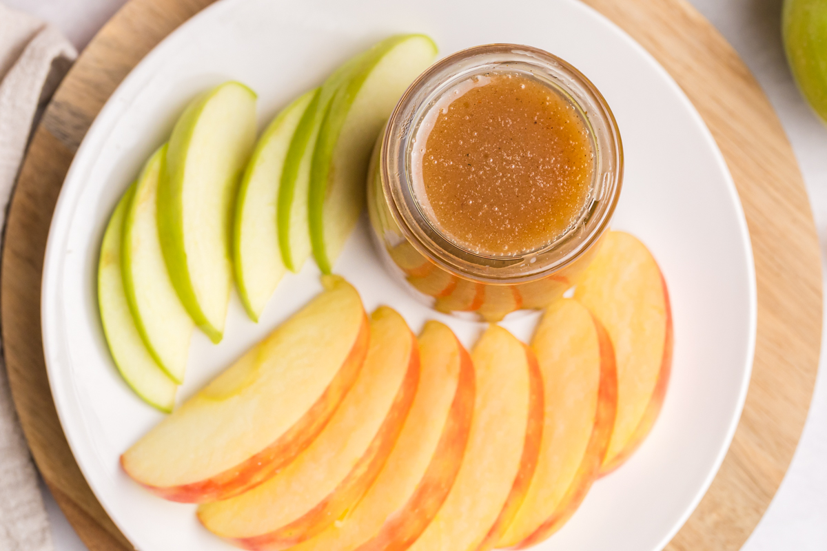 overhead shot of caramel sauce in jar on plate of sliced apples