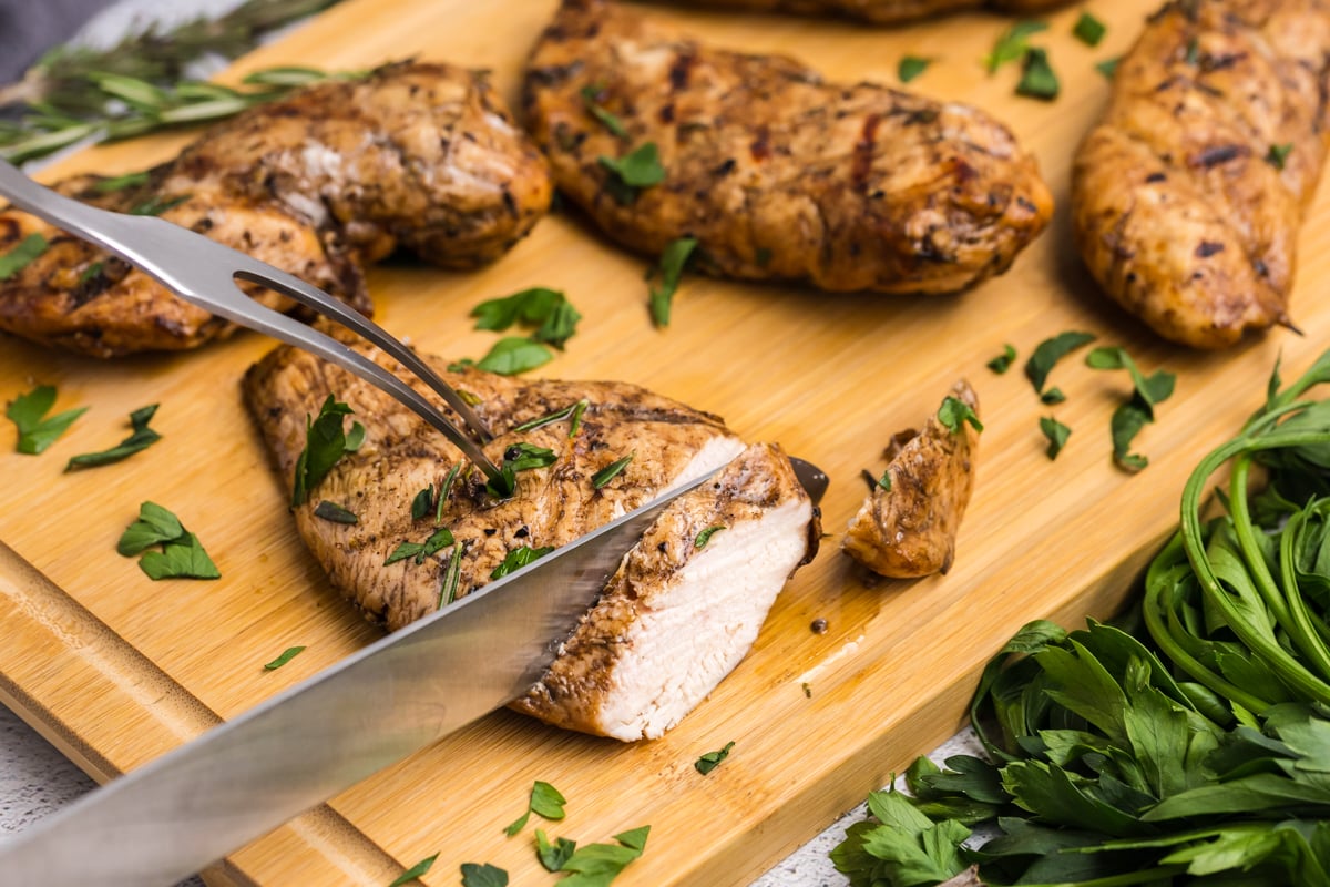 knife and fork cutting marinaded chicken on cutting board