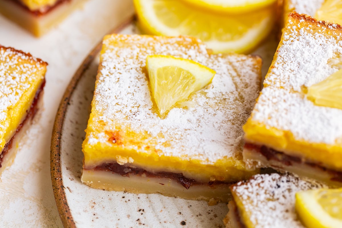 close up of cranberry lemon bars on plate topped with fresh lemon