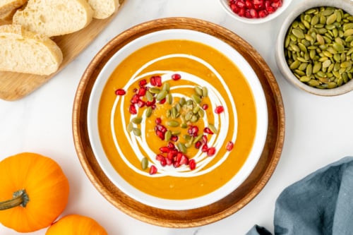 overhead shot of bowl of pumpkin soup topped with pomegranates and pepitas