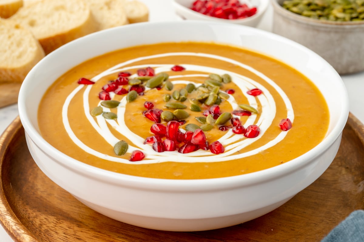 close up angled shot of bowl of creamy soup topped with pomegranate seeds and pepitas