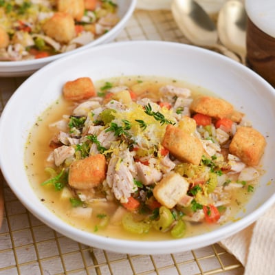 Bowl of quick chicken and wild rice soup with lemon zest, Parmesan, and croutons on a cozy linen.