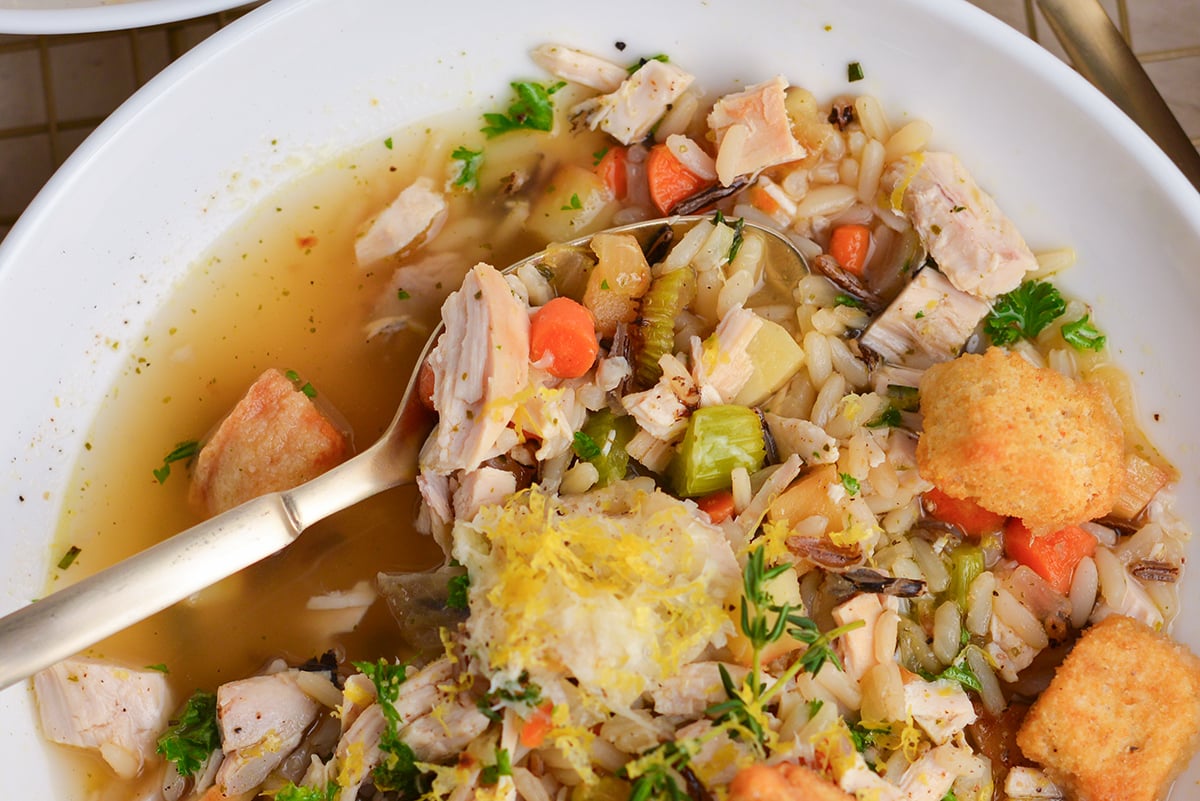 Spoon dipping into creamy-looking chicken and wild rice soup with rosemary and thyme.