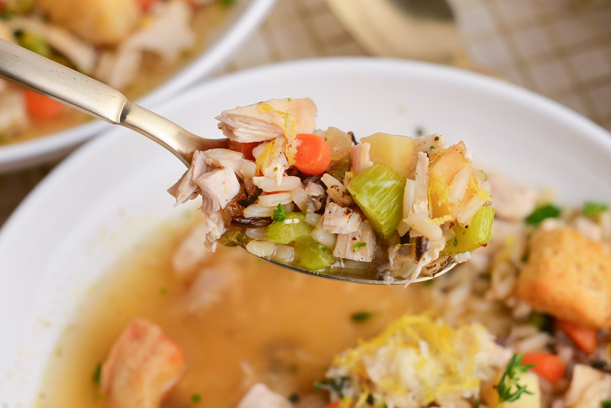 spoon lifting chicken and wild rice soup from a white bowl, showing hearty grains and herbs