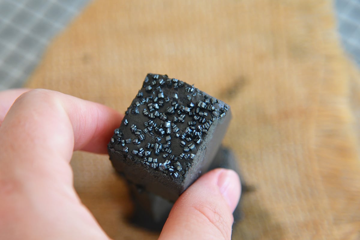 Hand reaching in for a piece of black fudge with sprinkles on top