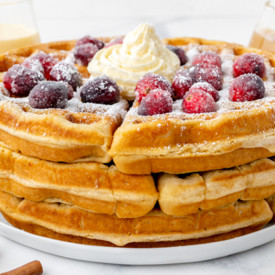 angled shot of stack of eggnog waffles topped with cranberries and whipped cream