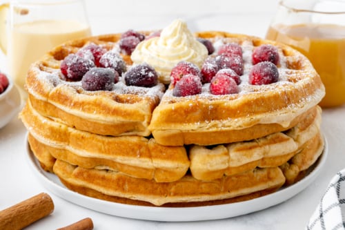 angled shot of stack of eggnog waffles topped with cranberries and whipped cream