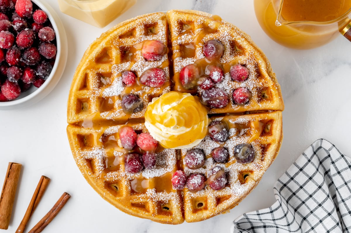 overhead shot of waffle topped with syrup, cranberries and whipped cream