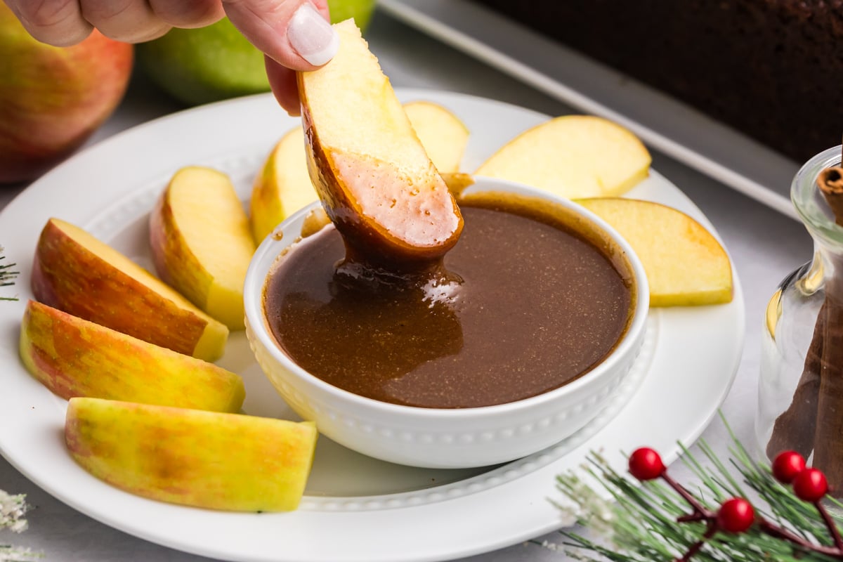 hand dipping apple slice into gingerbread caramel sauce
