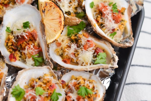 angled shot of cooked oysters on tray with lemon wedges