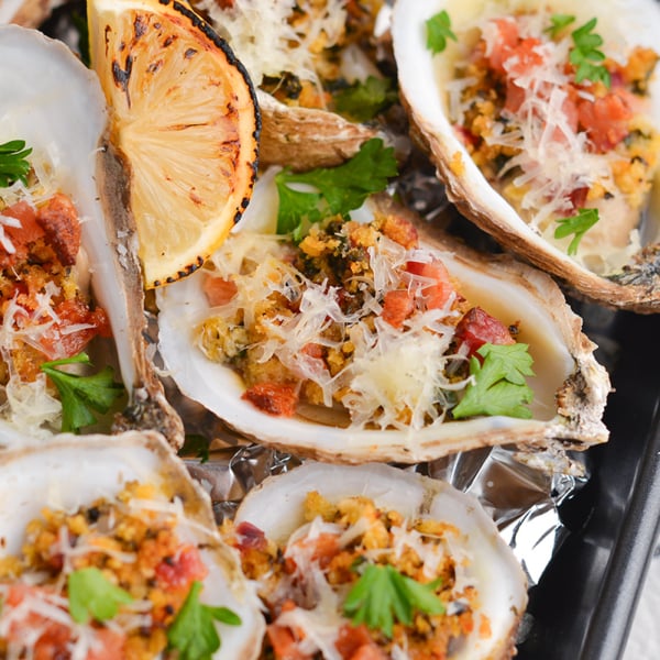 angled shot of cooked oysters on tray with lemon wedges