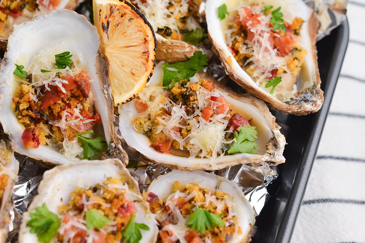 angled shot of cooked oysters on tray with lemon wedges