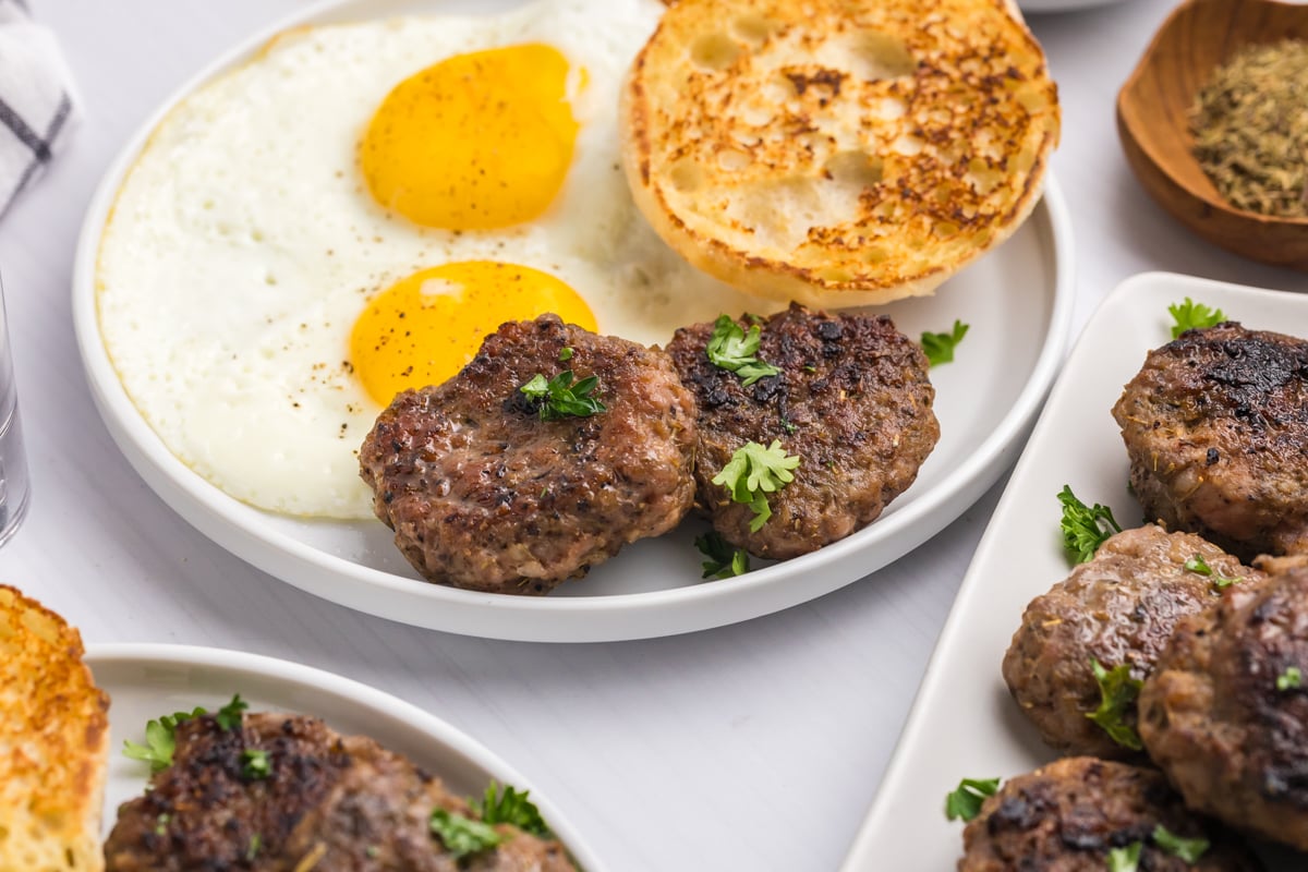 angled shot of two breakfast sausage patties on plate with eggs and english muffin