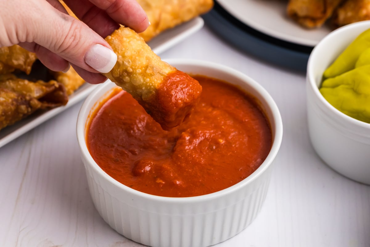 hand dipping egg roll into marinara sauce
