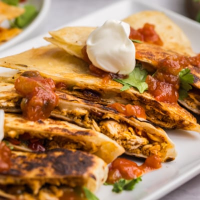 angled shot of platter of quesadillas topped with salsa and sour cream