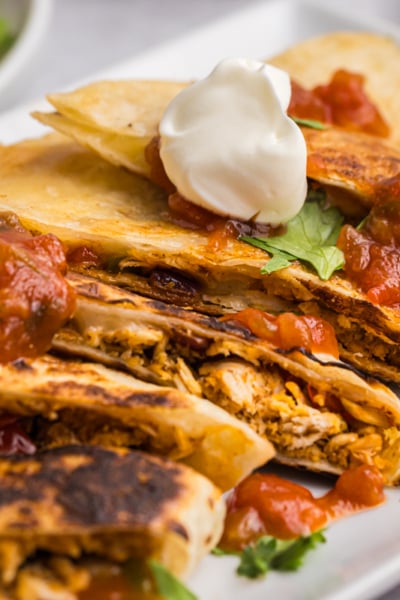 angled shot of platter of quesadillas topped with salsa and sour cream