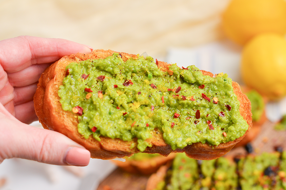 hand holding crostini with pea mash and red pepper flakes