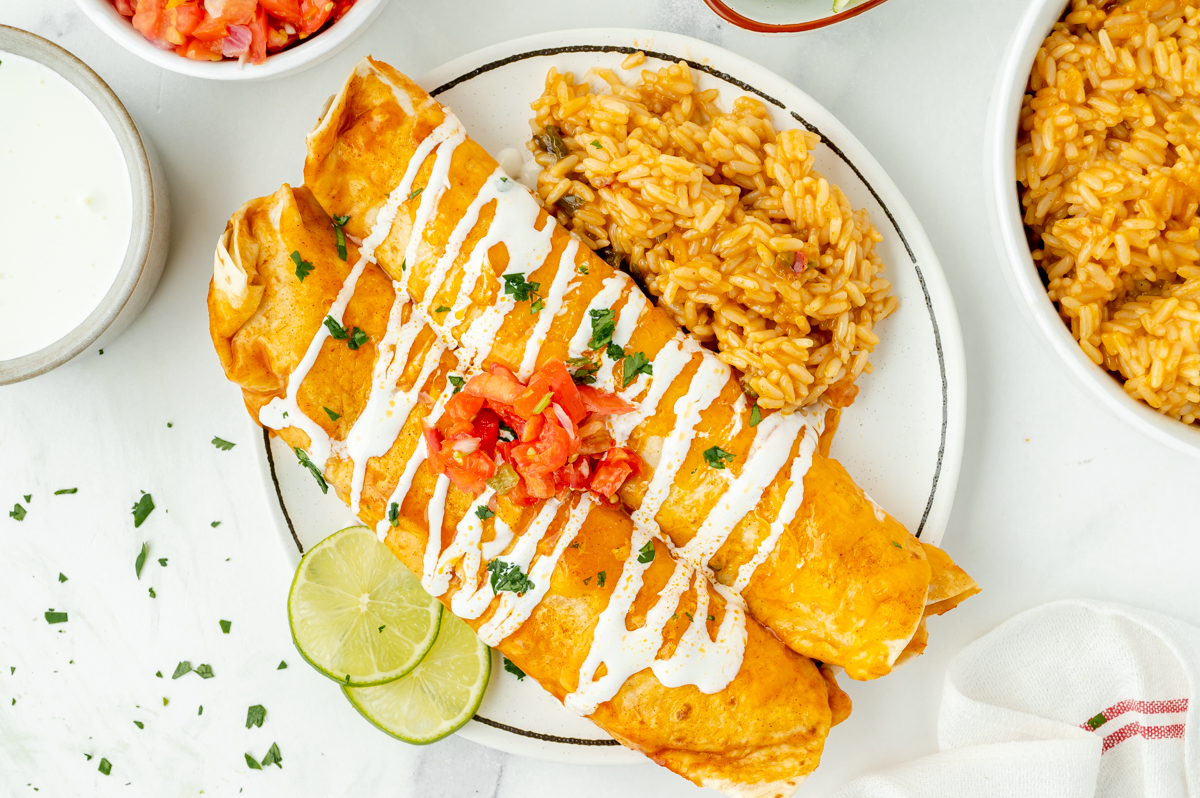 overhead shot of two burritos on plate with rice and limes