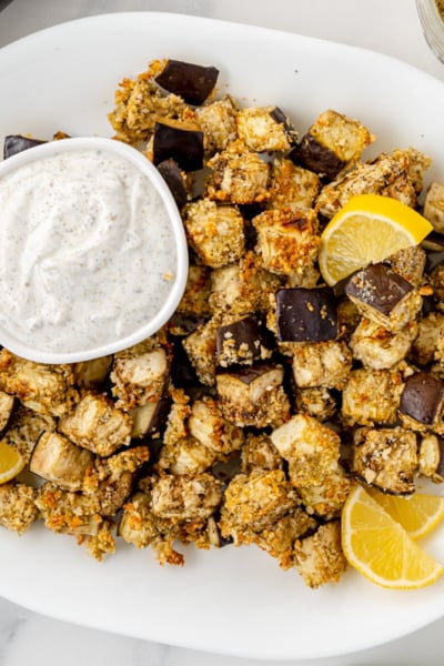 overhead shot of eggplant bites on platter with dipping sauce and lemon slices