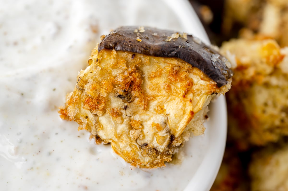 close up of eggplant bite dipping into bowl of sauce