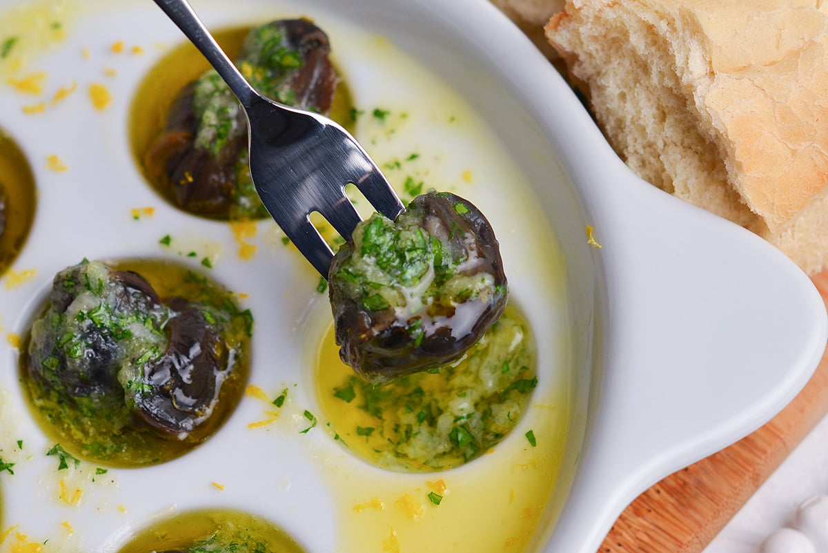seafood fork picking up an escargot drenched in garlic parsley butter