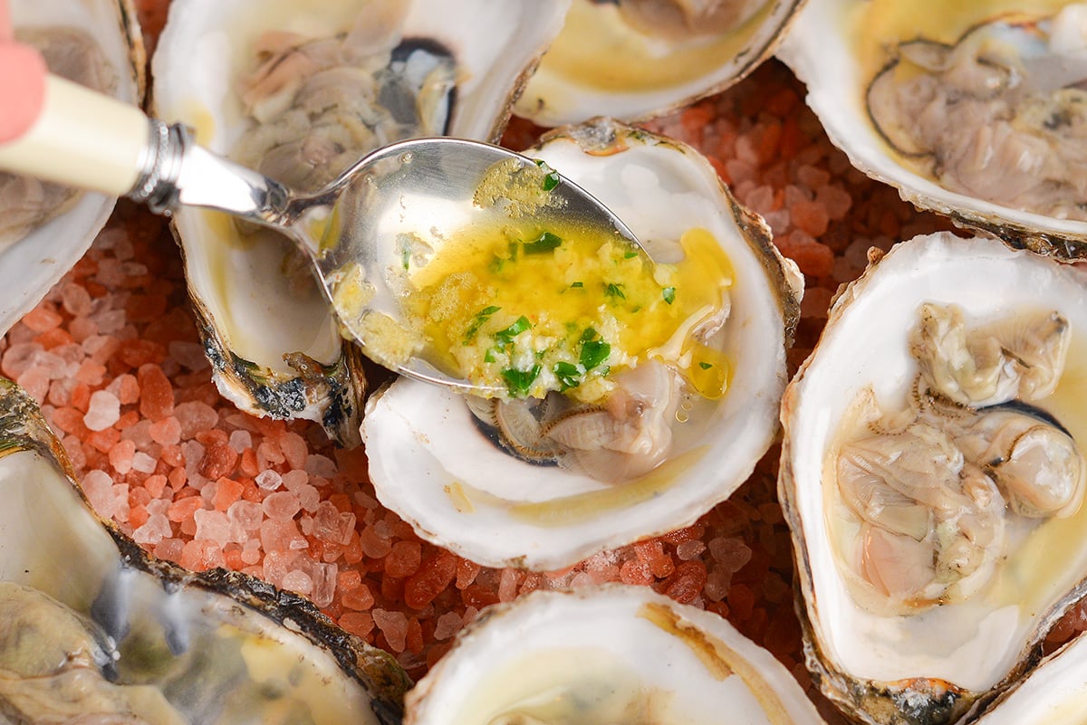 spoon adding garlic butter to oysters