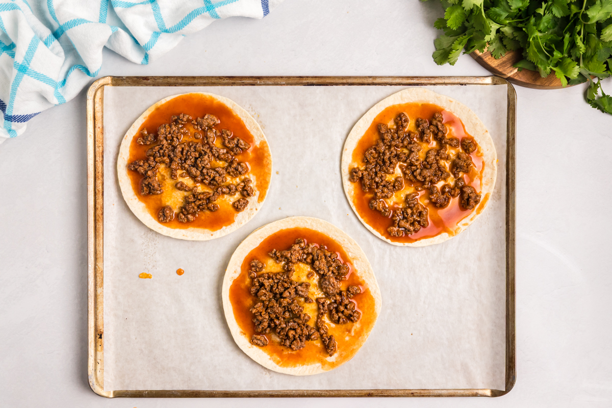 overhead shot of ground beef and taco sauce on tortillas
