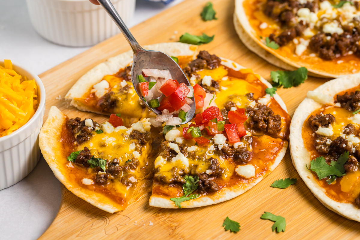 spoon adding pico de gallo to mexican pizza