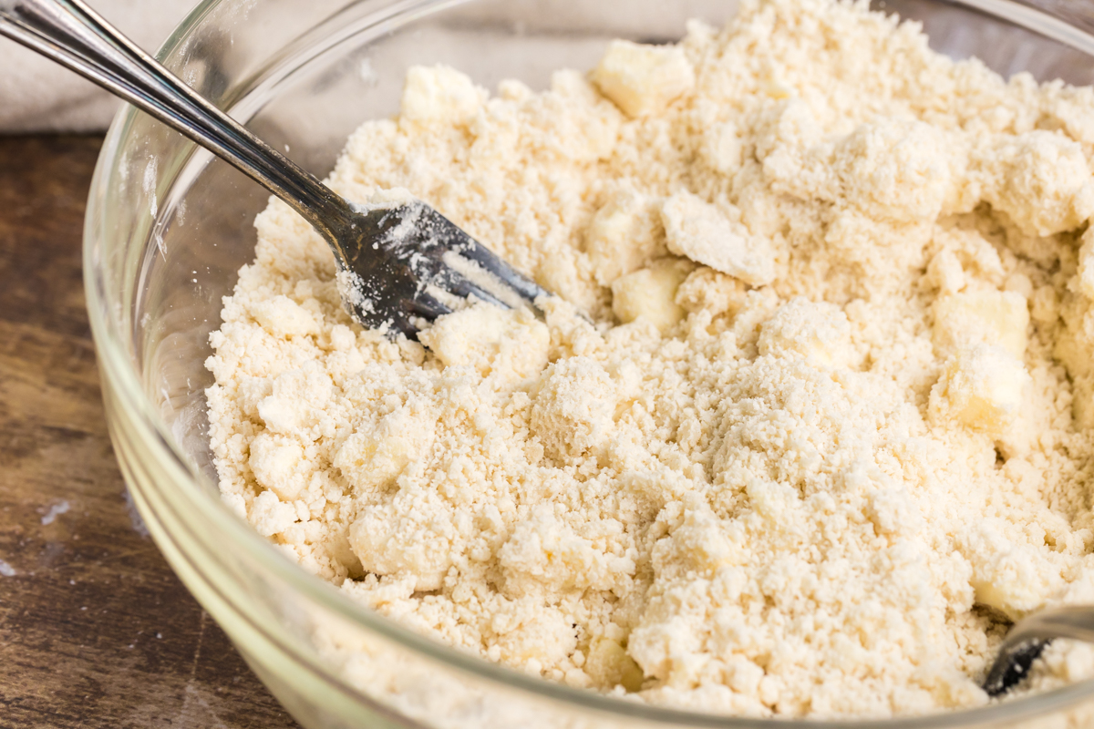 angled shot of pie crust ingredients mixing in bowl with fork