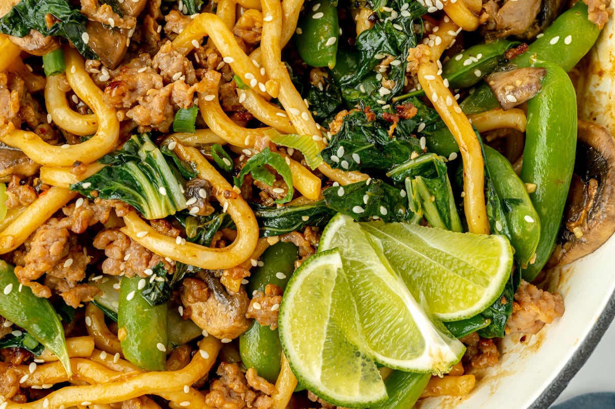 close up of sliced limes in pan of stir fry noodles
