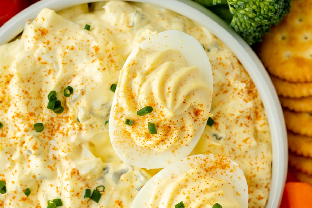 close up shot of deviled egg in bowl of dip