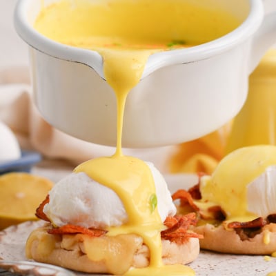 close up of sauce pouring over eggs benedict