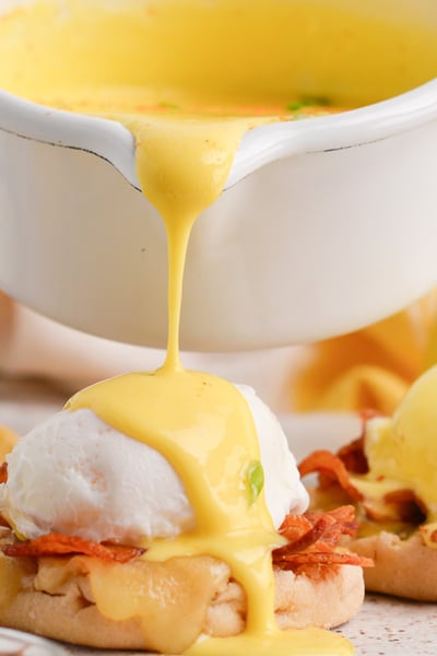 close up of sauce pouring over eggs benedict