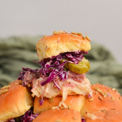 slider sandwich piled high with a pickle, coleslaw, corned beef and cheese