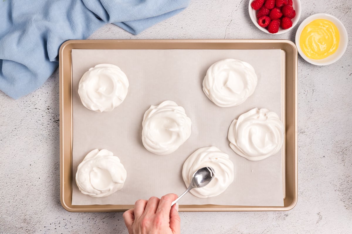 spoon making wells in meringues on baking sheet