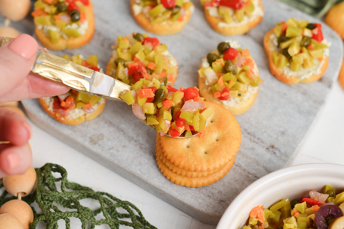 small spoon placing tapenade on a stack of crackers