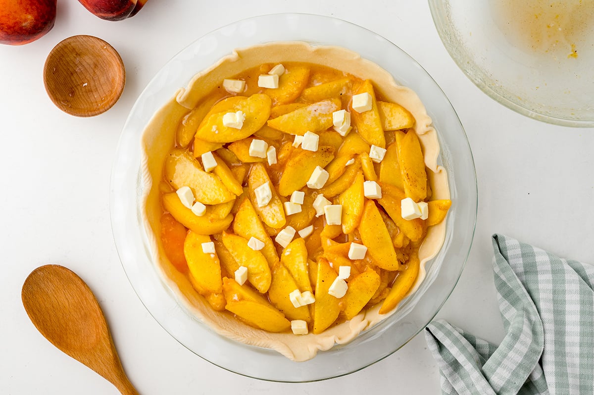 overhead shot of butter dotting filling of unbaked peach pie