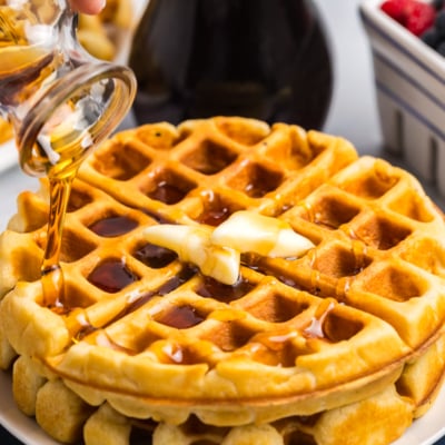 angled shot of syrup pouring over stack of homemade waffles