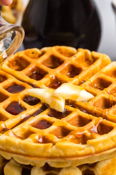 angled shot of syrup pouring over stack of homemade waffles