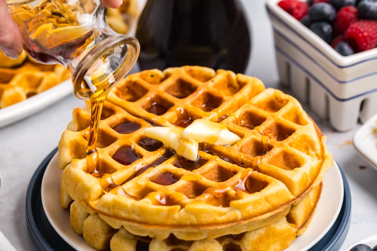 angled shot of syrup pouring over stack of homemade waffles
