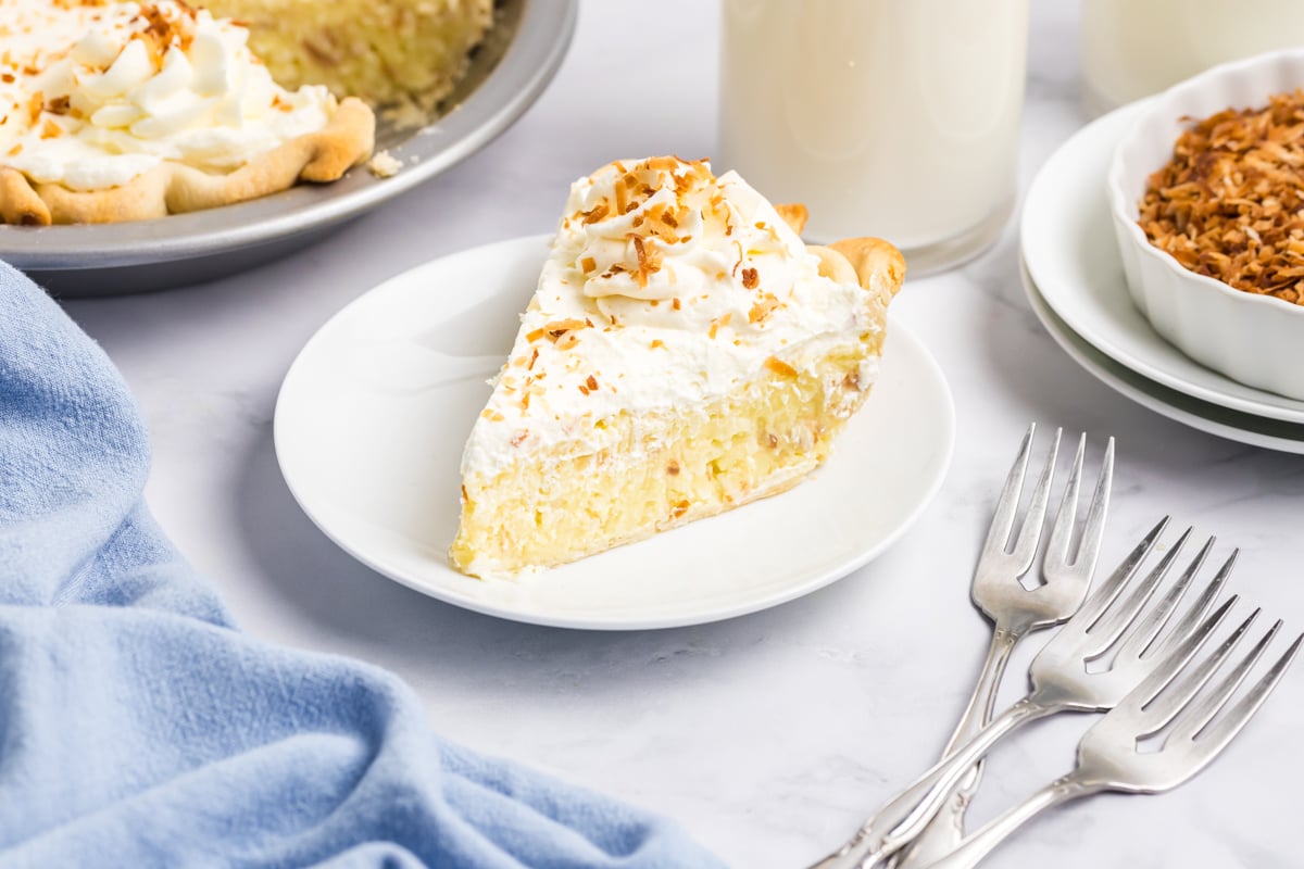 slice of coconut cream pie on dessert plate with whipped cream and toasted coconut