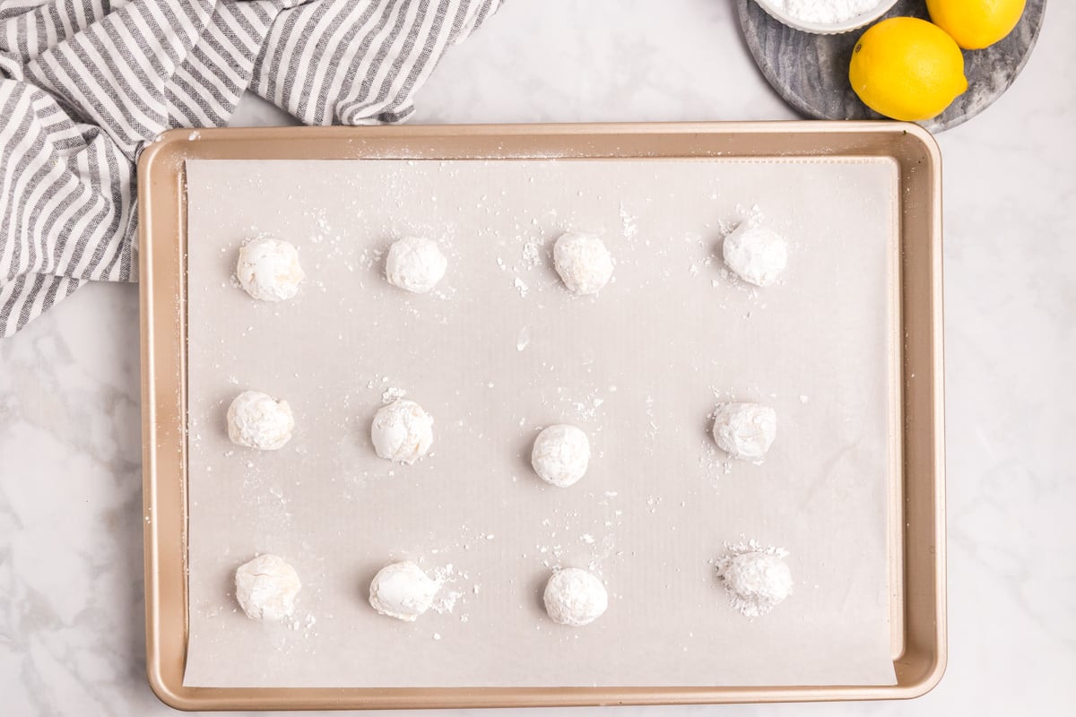lemon cooler cookie dough balls rolled in powdered sugar on baking sheet