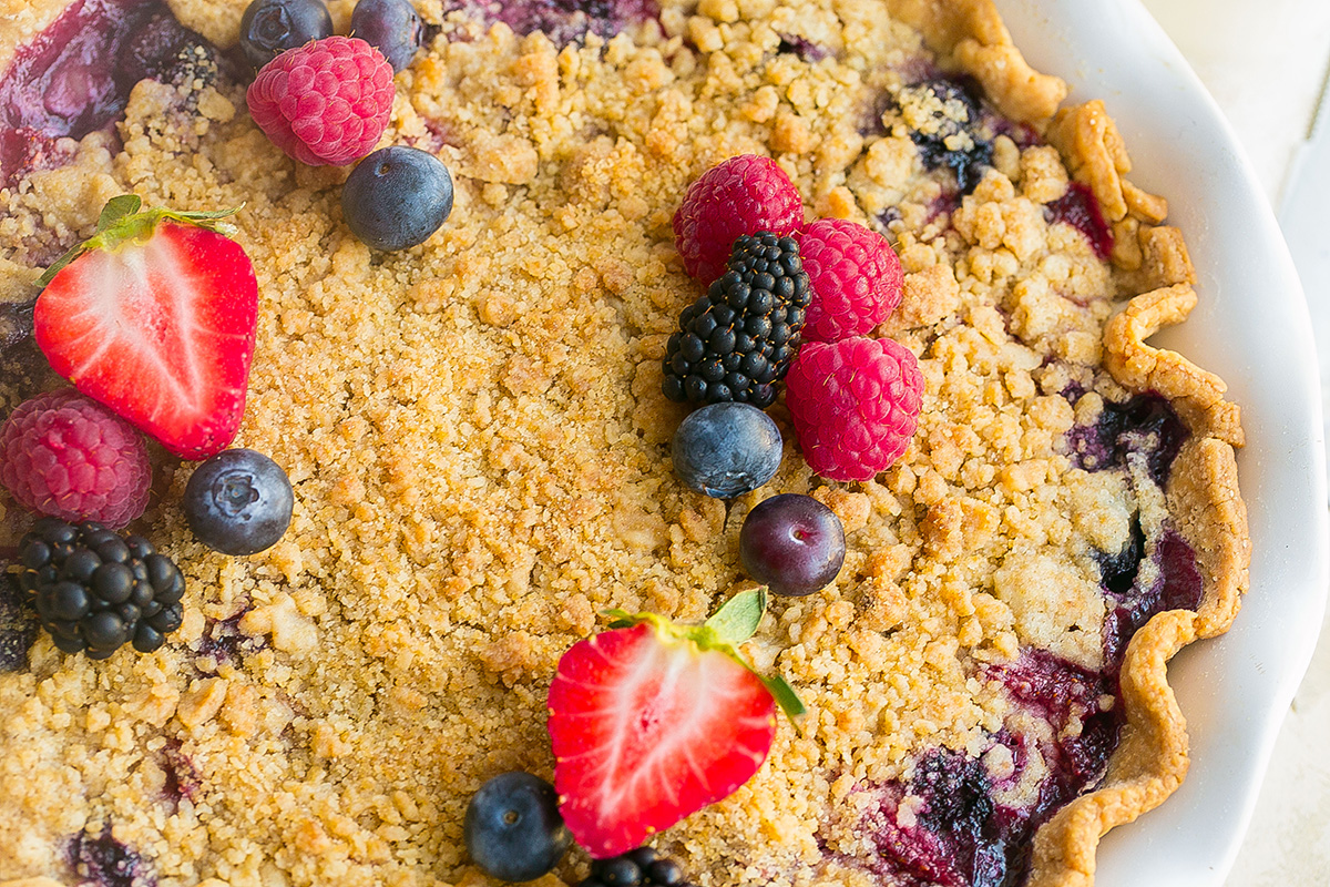 Close-up of baked mixed berry pie with golden crumb topping and fresh berries
