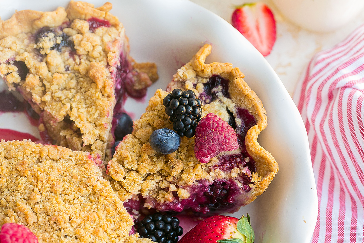 Mixed berry pie sliced in the pie pan showing juicy berry filling and crumb topping