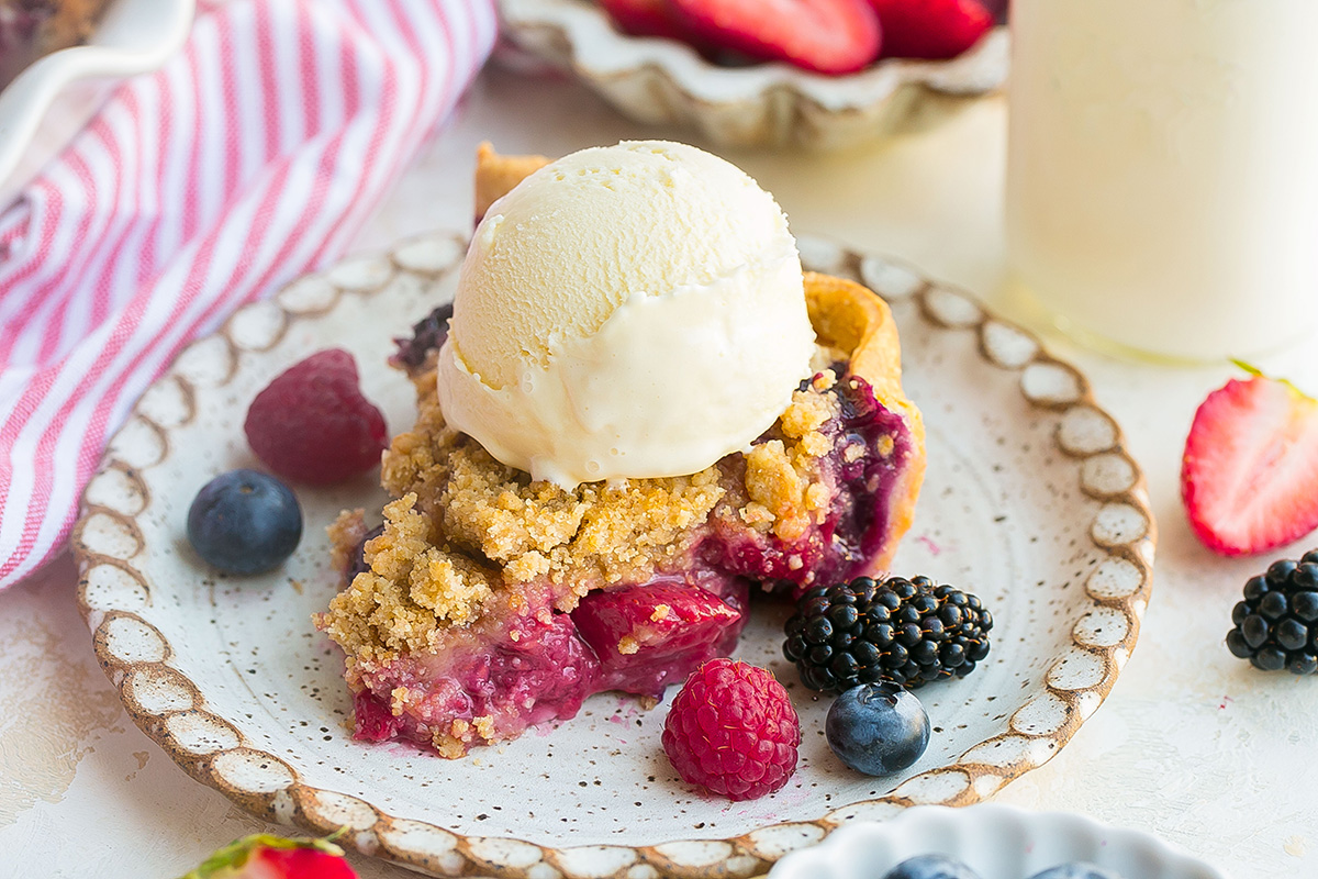 Slice of mixed berry pie with crumb topping served on a plate with vanilla ice cream