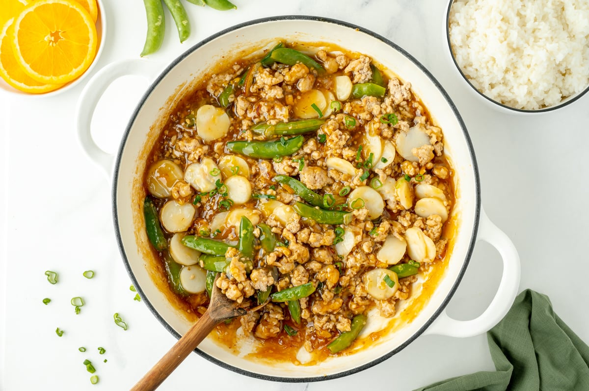 overhead shot of pot of ground orange chicken with wooden spoon