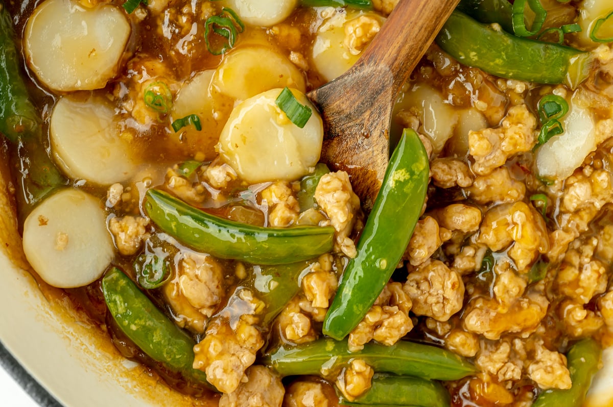 close up of wooden spoon in pot of ground orange chicken
