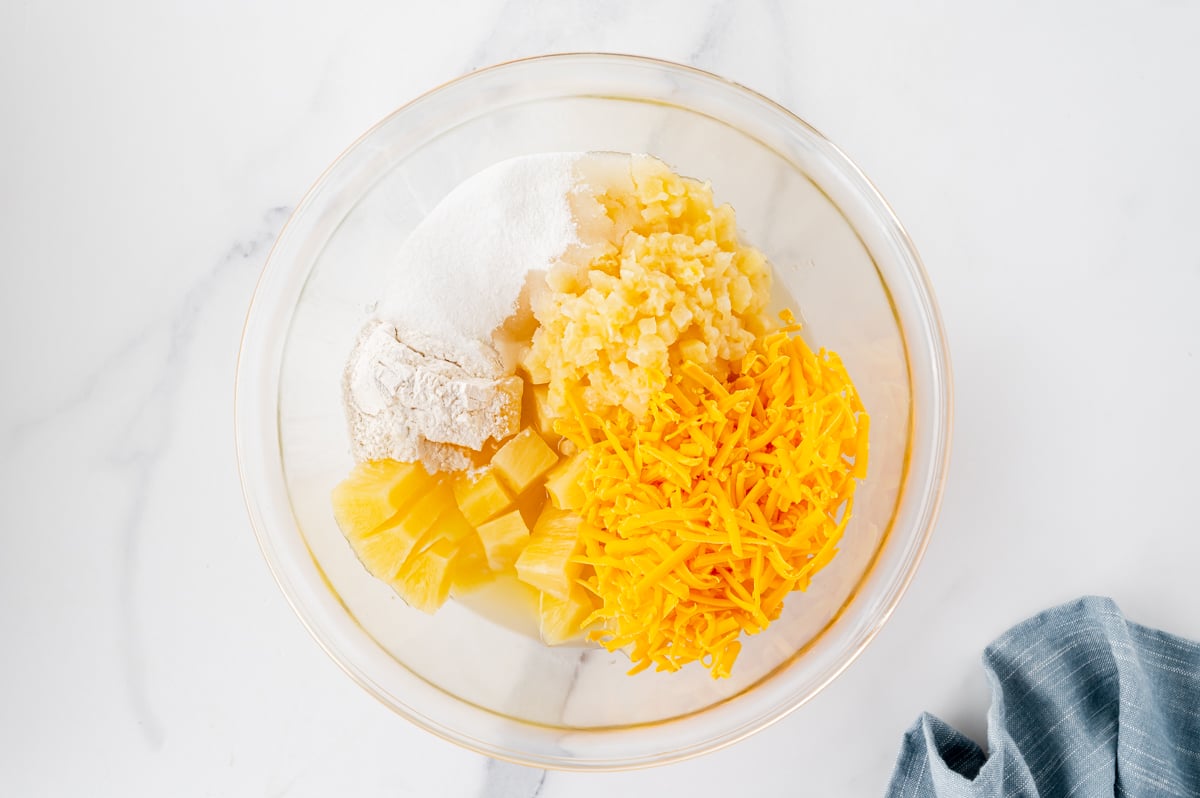 Ingredients for pineapple casserole including canned pineapple, cheddar cheese, sugar, flour, butter, and Ritz crackers